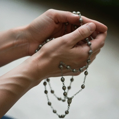 Person holding rosary beads, symbolizing prayer and spiritual connection